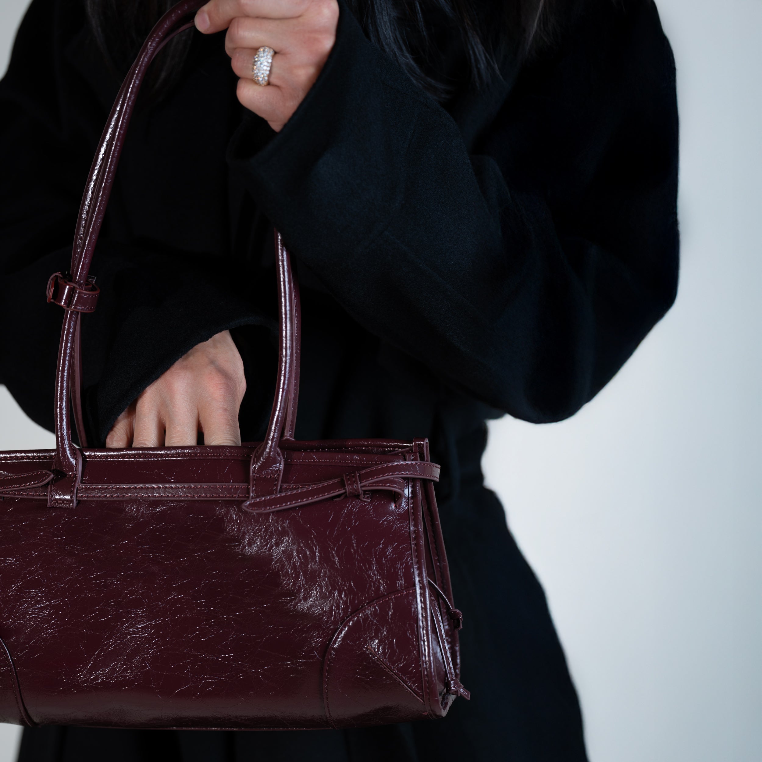 personne qui cherche dans son sac à main forme baguette femme en cuir verni bordeaux vintage avec un manteau noir avec une bague en diamant