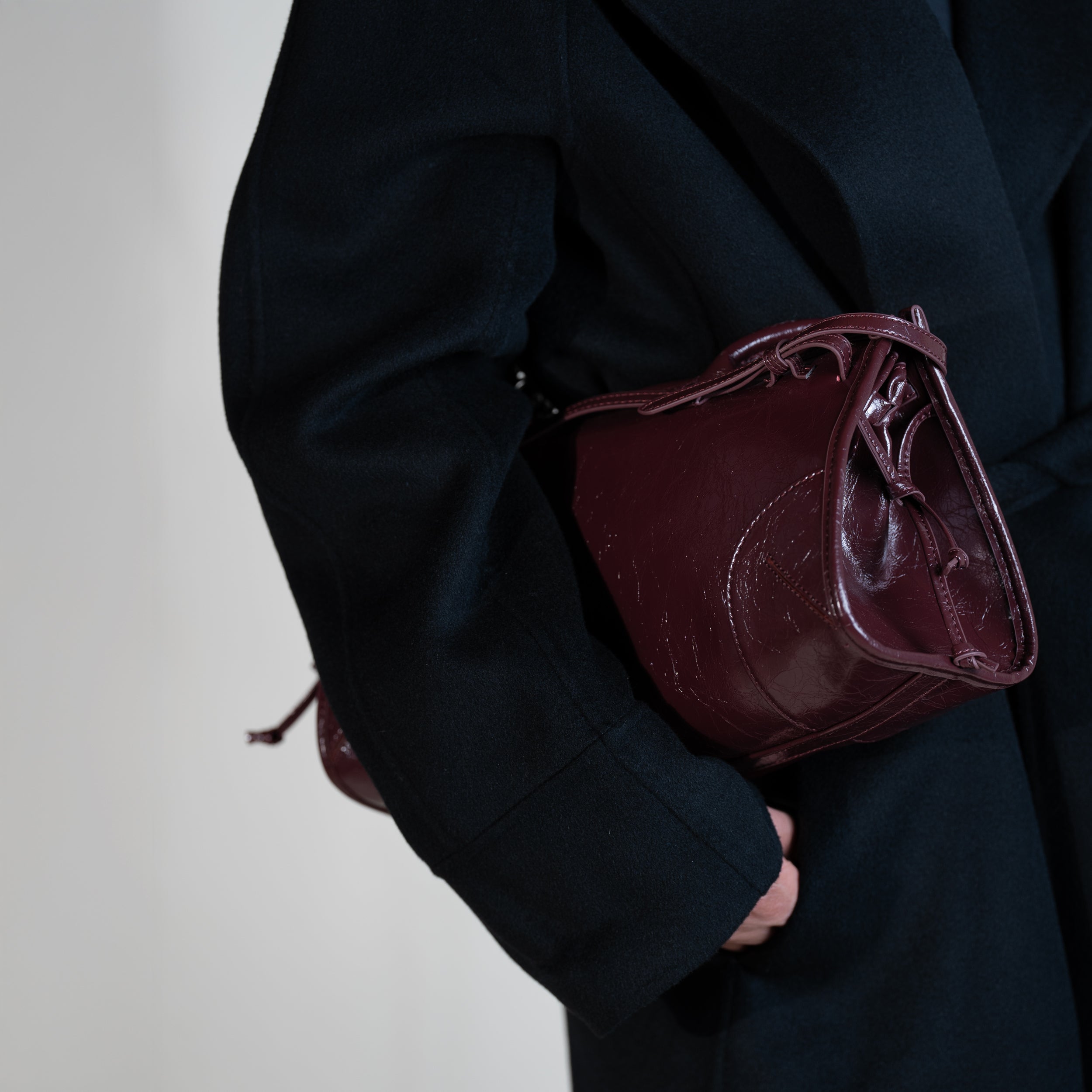 sac à main forme baguette femme en cuir verni bordeaux vintage porté sous le bras sur un manteau noir