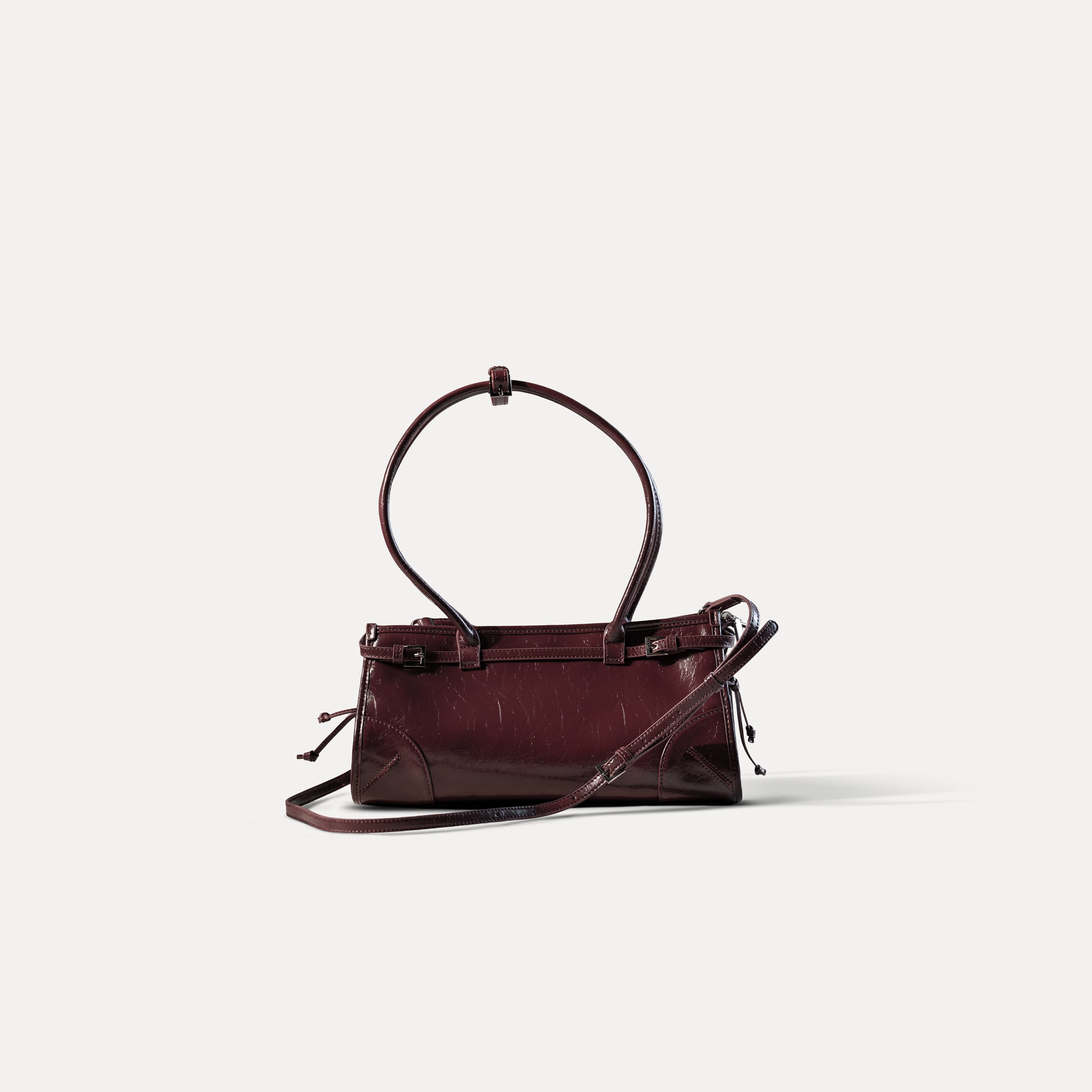 sac à main forme baguette pour femme en cuir verni bordeaux vintage avec bandoulière sur fond blanc