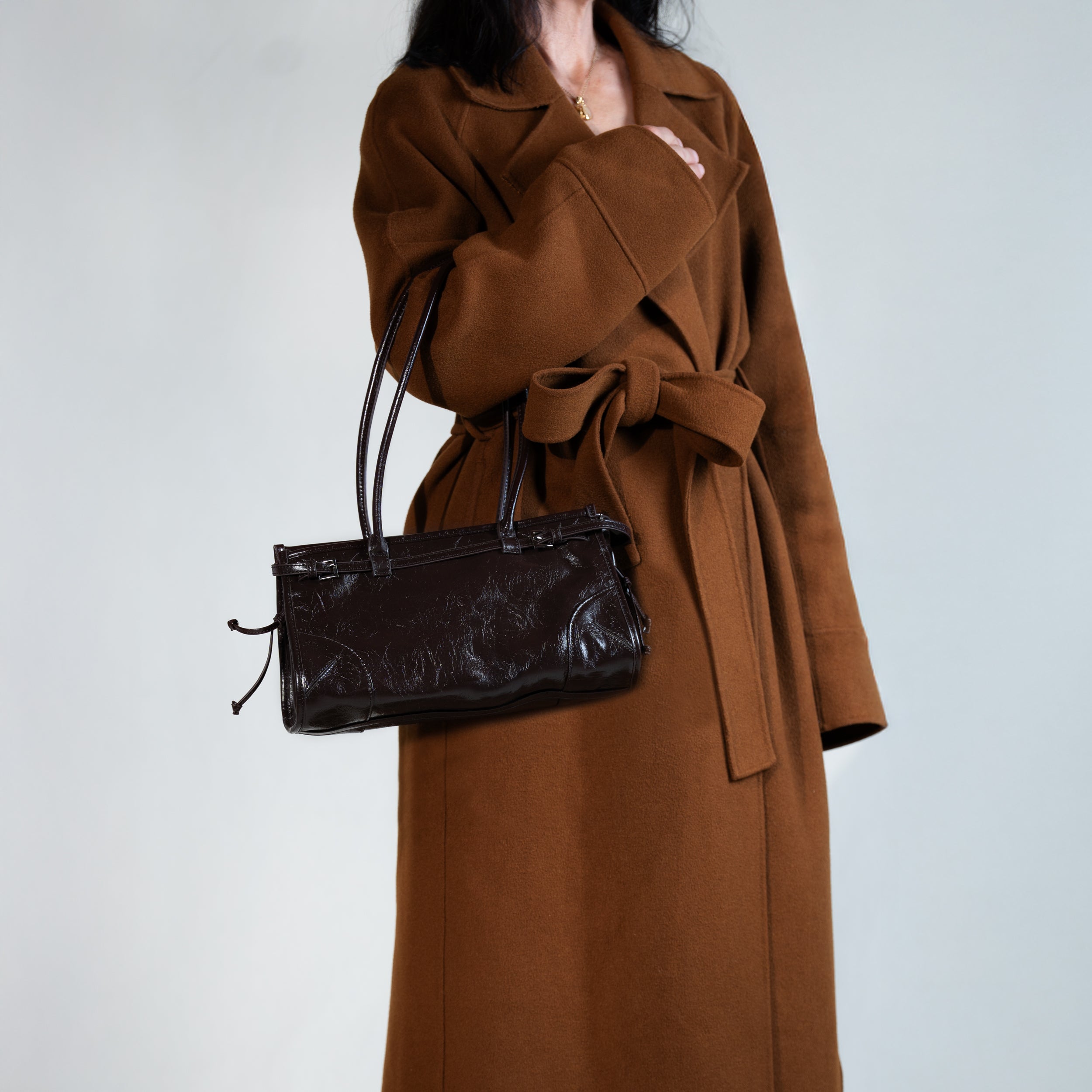 sac à main forme baguette femme en cuir verni marron porté au creux de bras sur un manteau camel