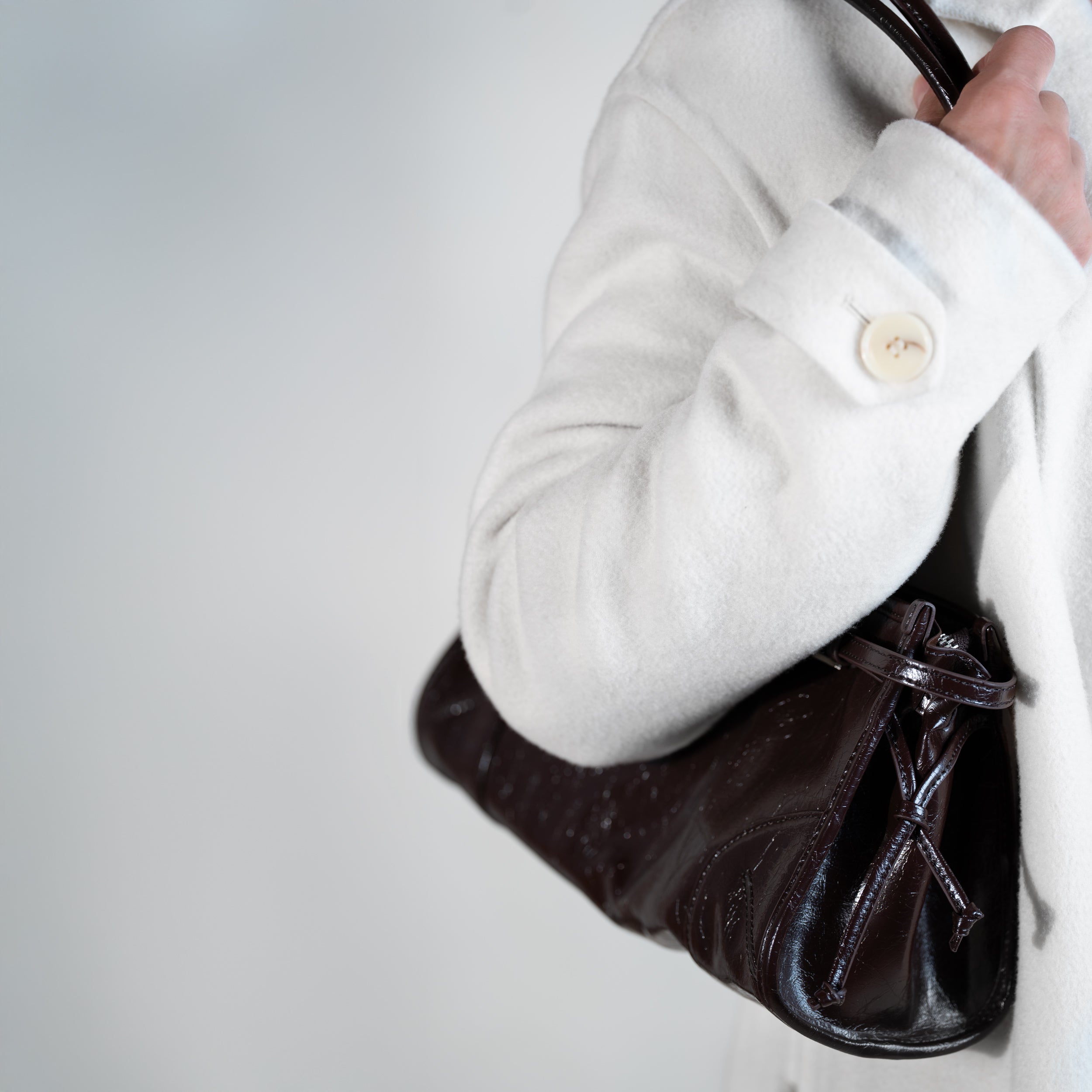 sac à main forme baguette femme en cuir verni marron porté à l'épaule sur un manteau blanc