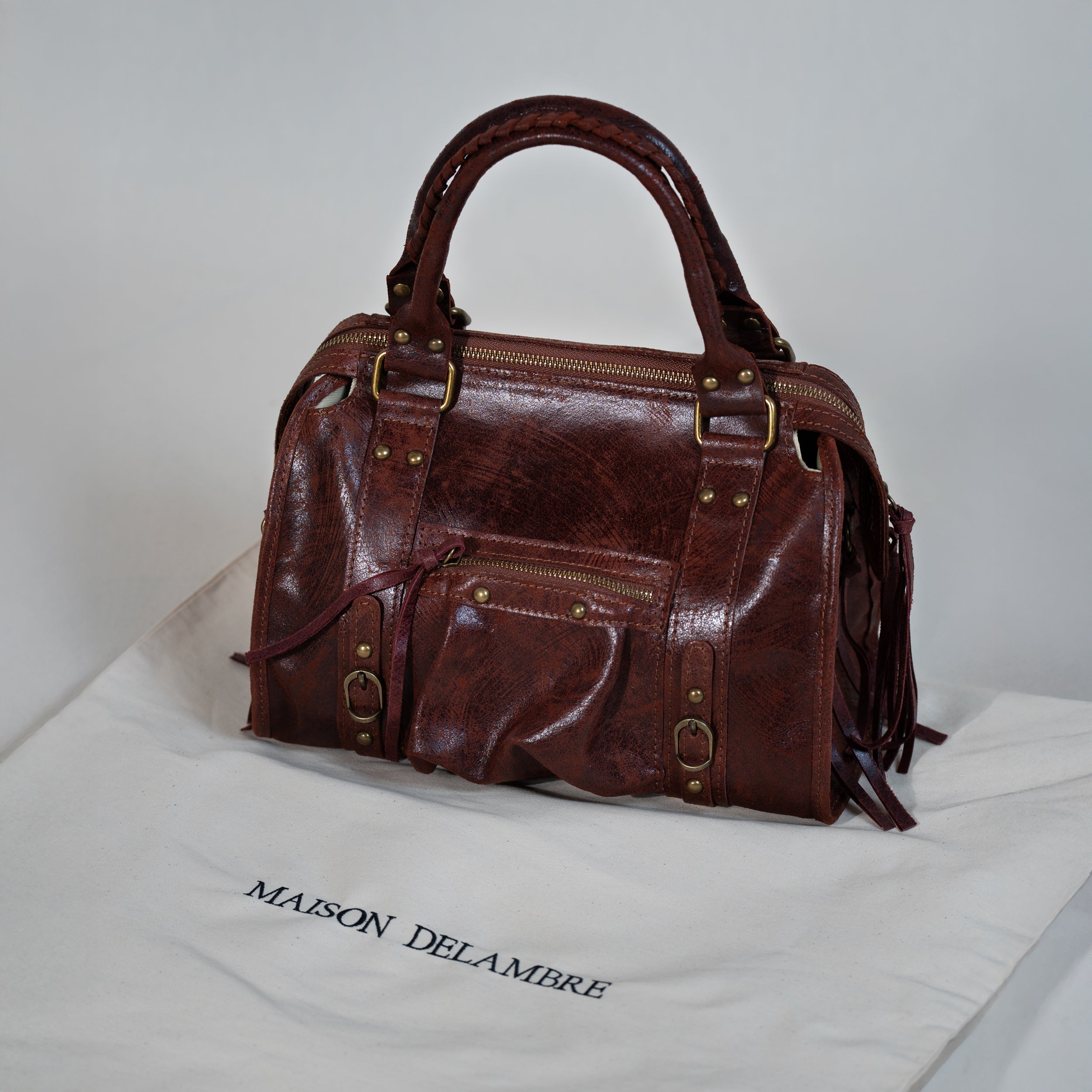 sac à main forme bowling vintage en cuir vieilli acajou posé sur son emballage en tissu beige brodé de la marque Maison Delambre