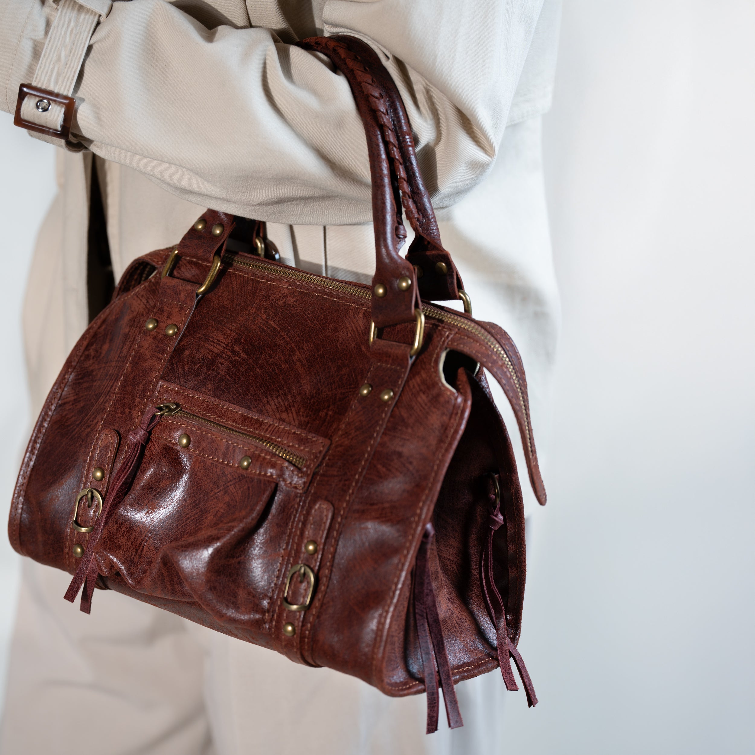 sac à main femme forme bowling vintage en cuir vieilli acajou souple porté main avec un trench beige et un pantalon tailleur beige