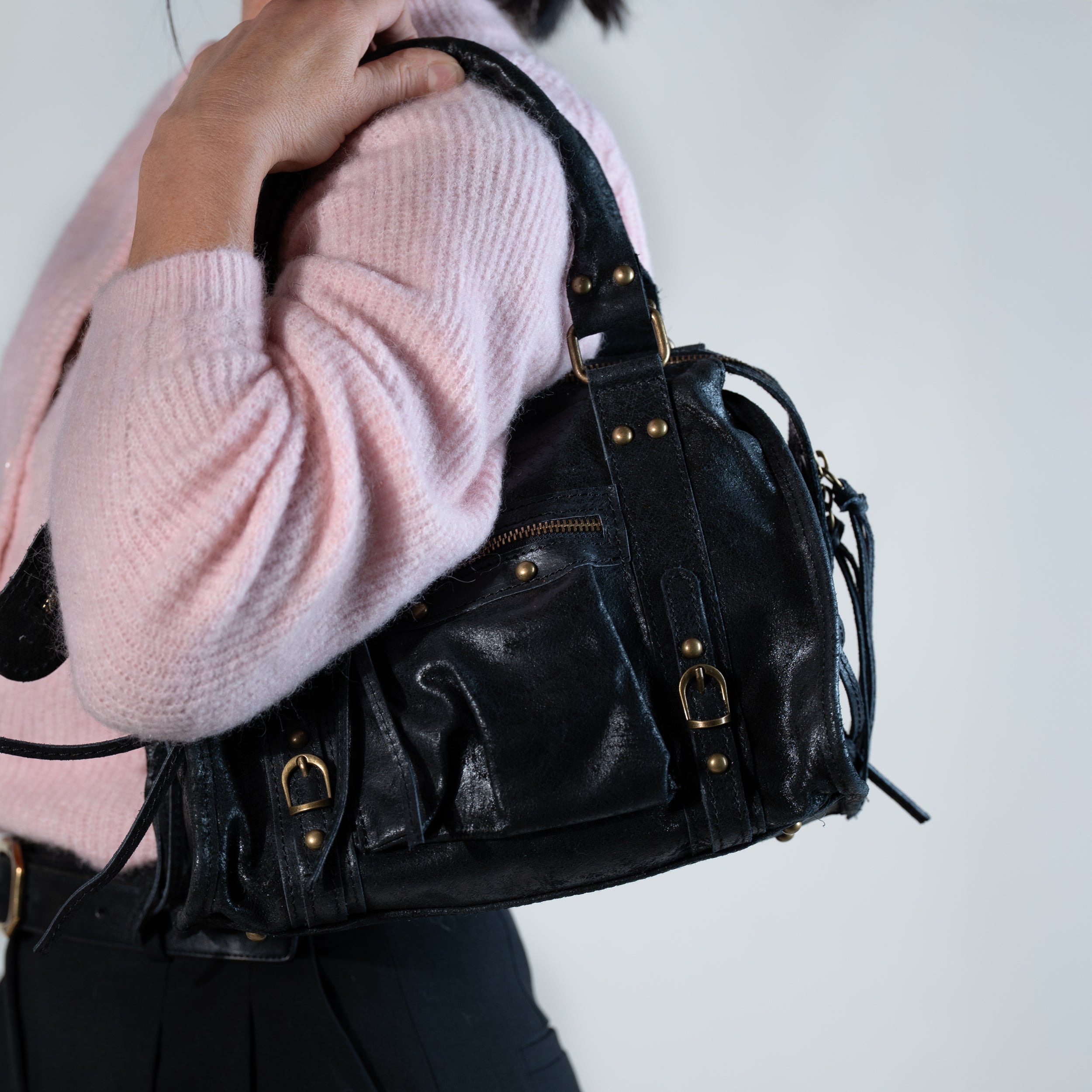 sac à main femme forme bowling vintage en cuir vieilli noir porté à l'épaule sur une tenue rose et noir