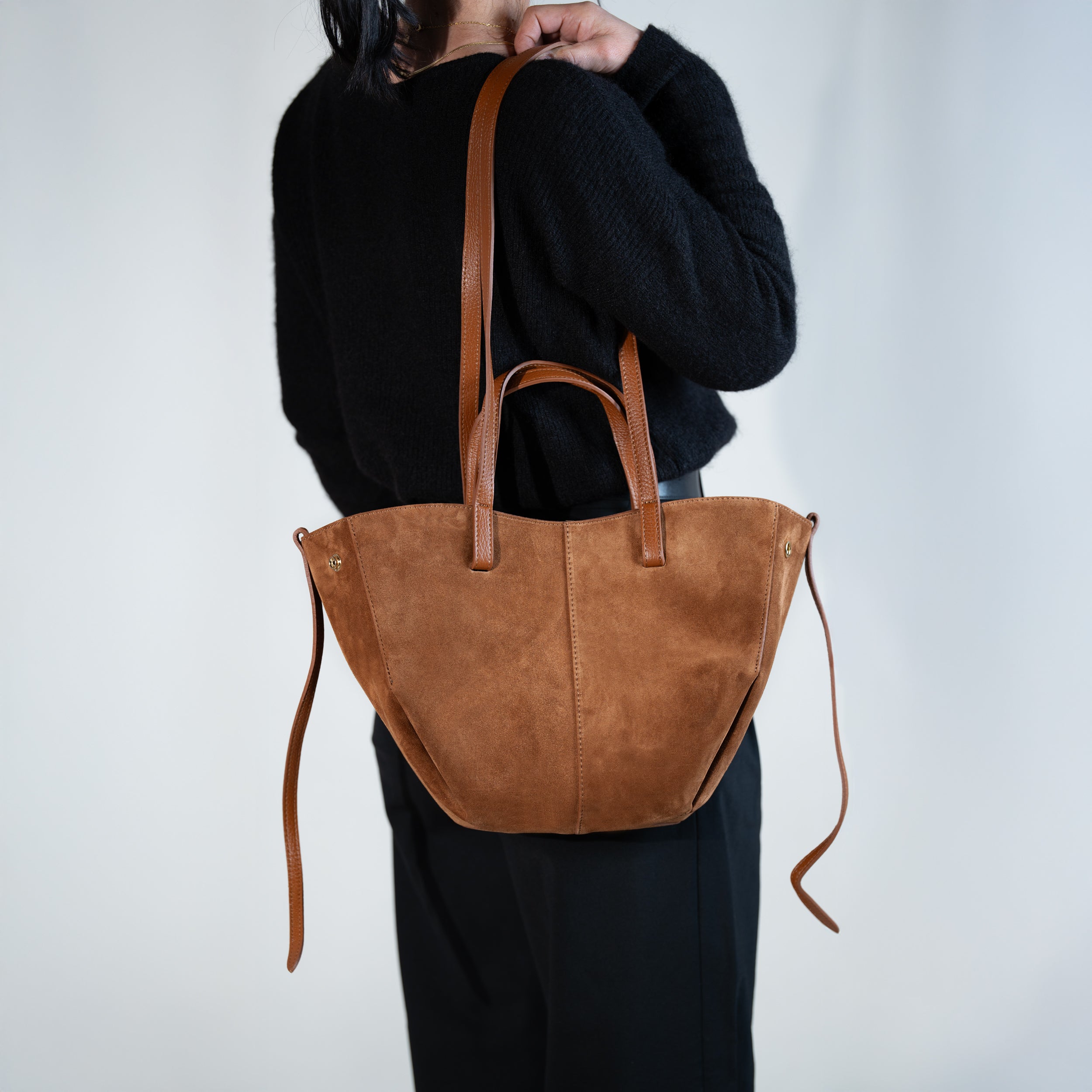 sac cabas forme trapèze en cuir suédé ou daim camel porté à l'épaule sur un pull noir et un pantalon noir