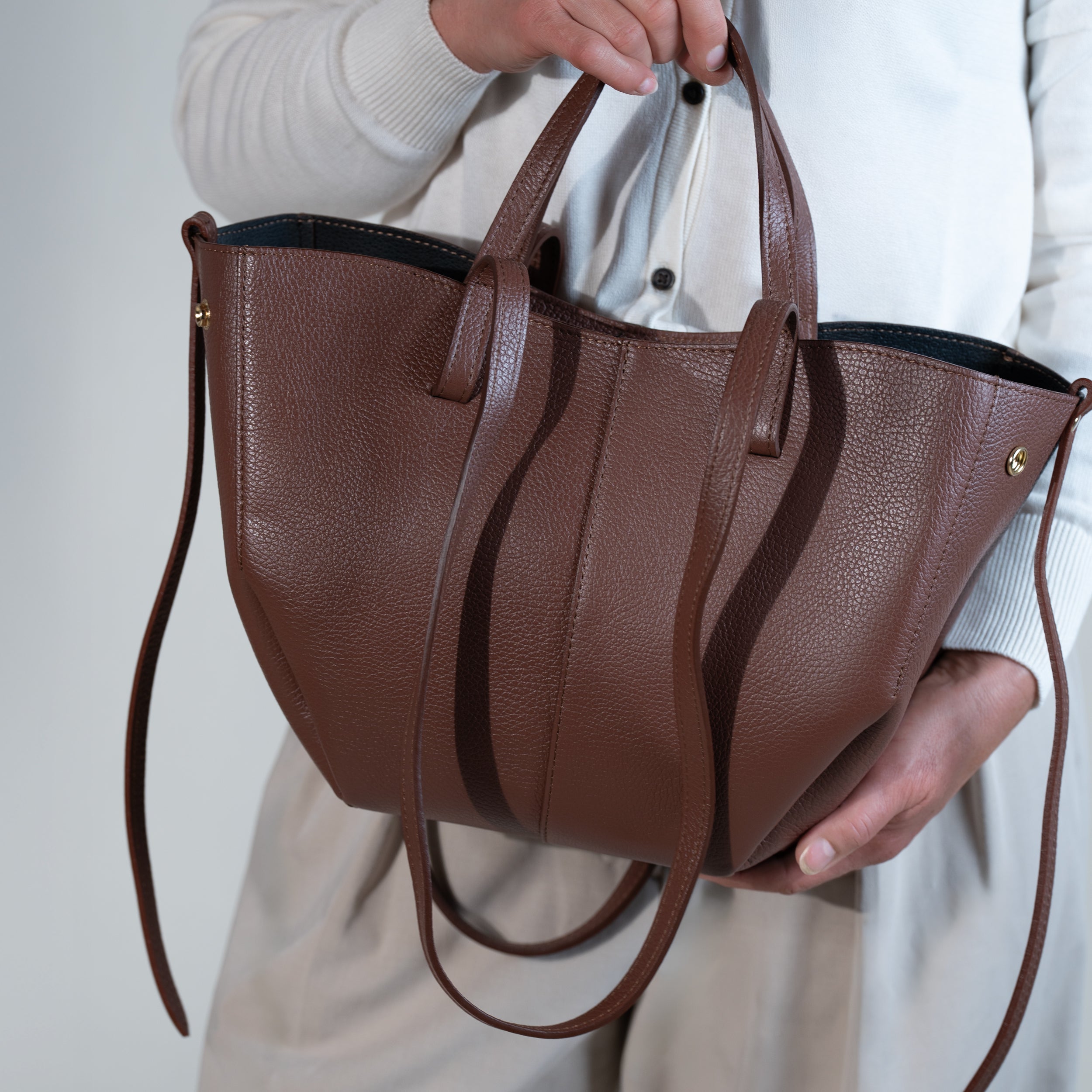 grand sac cabas pour femme forme trapèze en cuir lisse brun sur pull blanc et pantalon beige