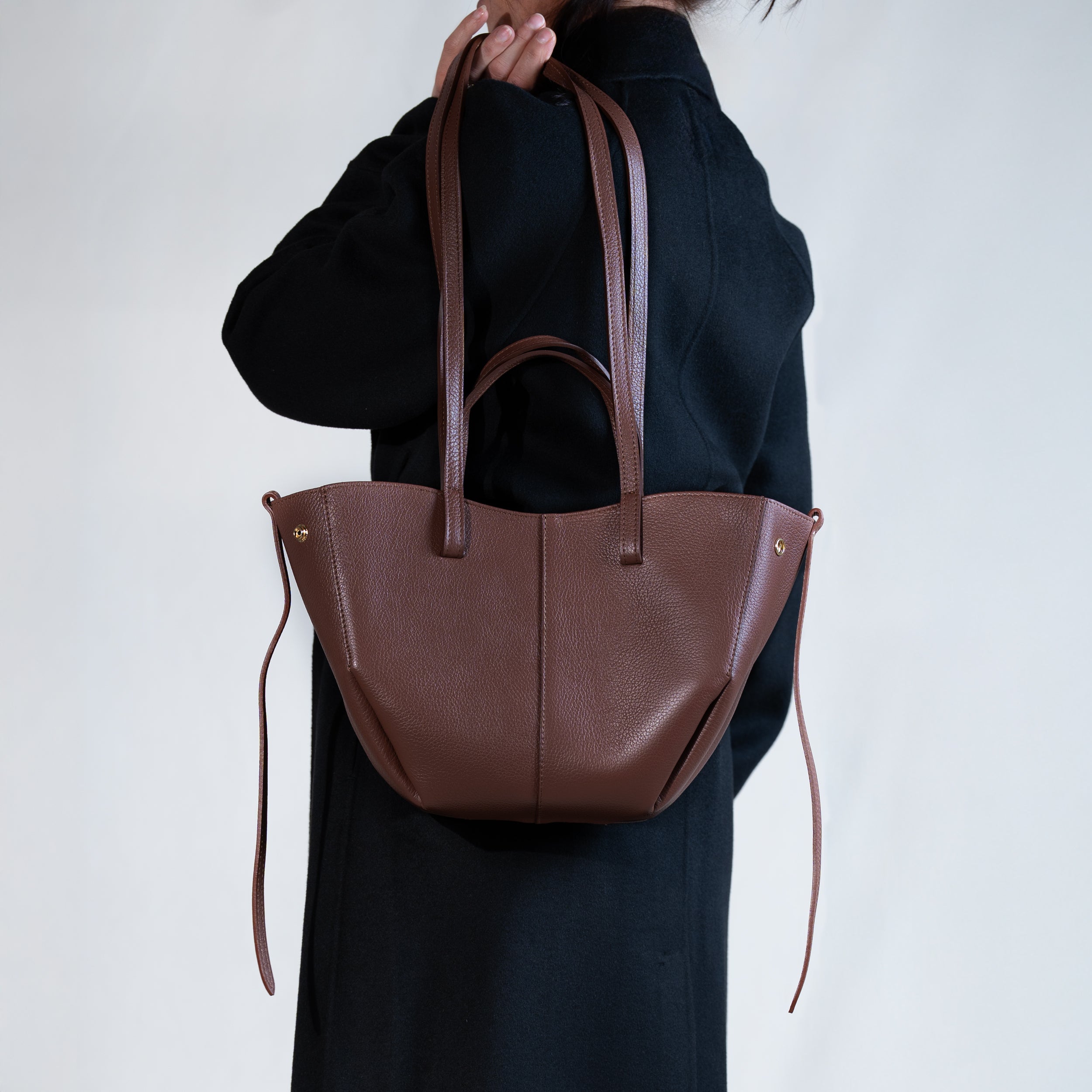 grand sac cabas pour femme forme trapèze en cuir lisse brun porté épaule sur manteau noir