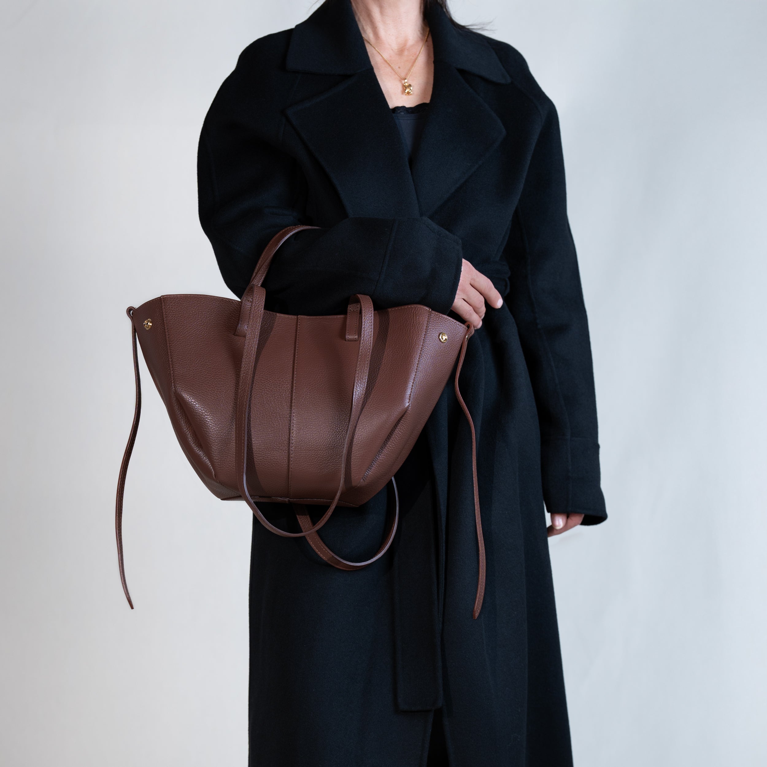 grand sac cabas pour femme forme trapèze en cuir lisse brun porté creux de bras sur manteau noir