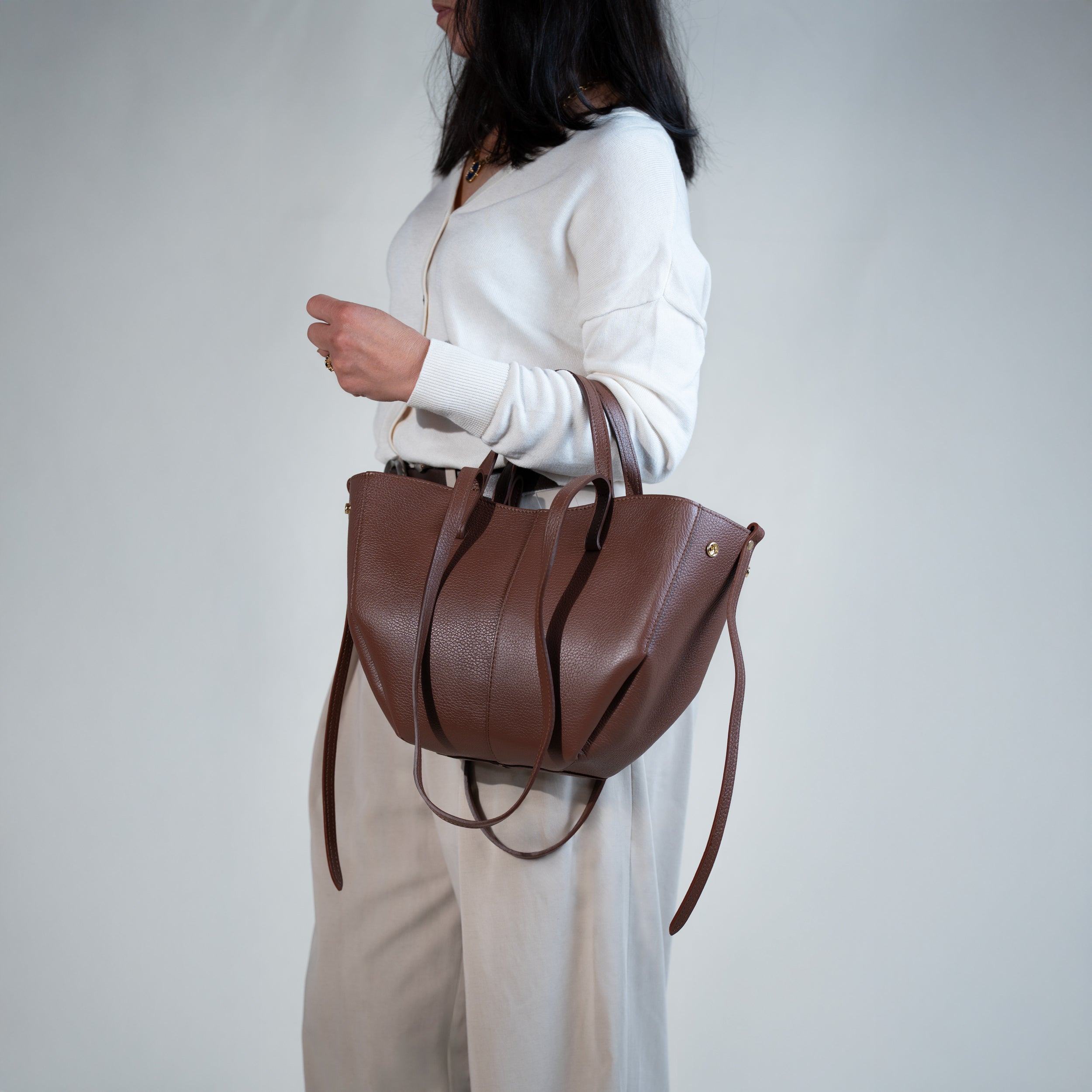 grand sac cabas pour femme forme trapèze en cuir lisse brun porté creux de bras sur pull blanc et pantalon beige