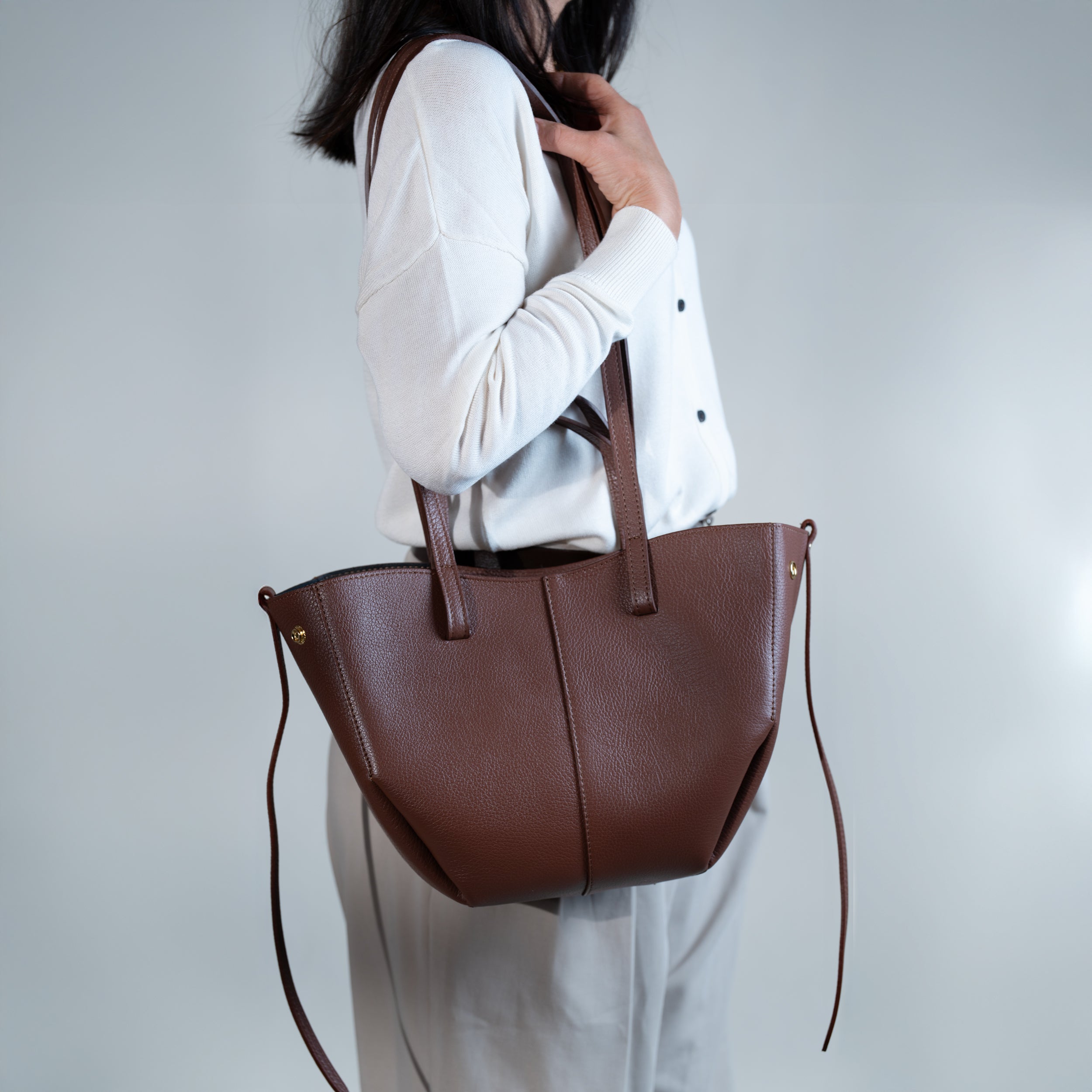 grand sac cabas pour femme forme trapèze en cuir lisse brun porté épaule sur pull blanc et pantalon beige