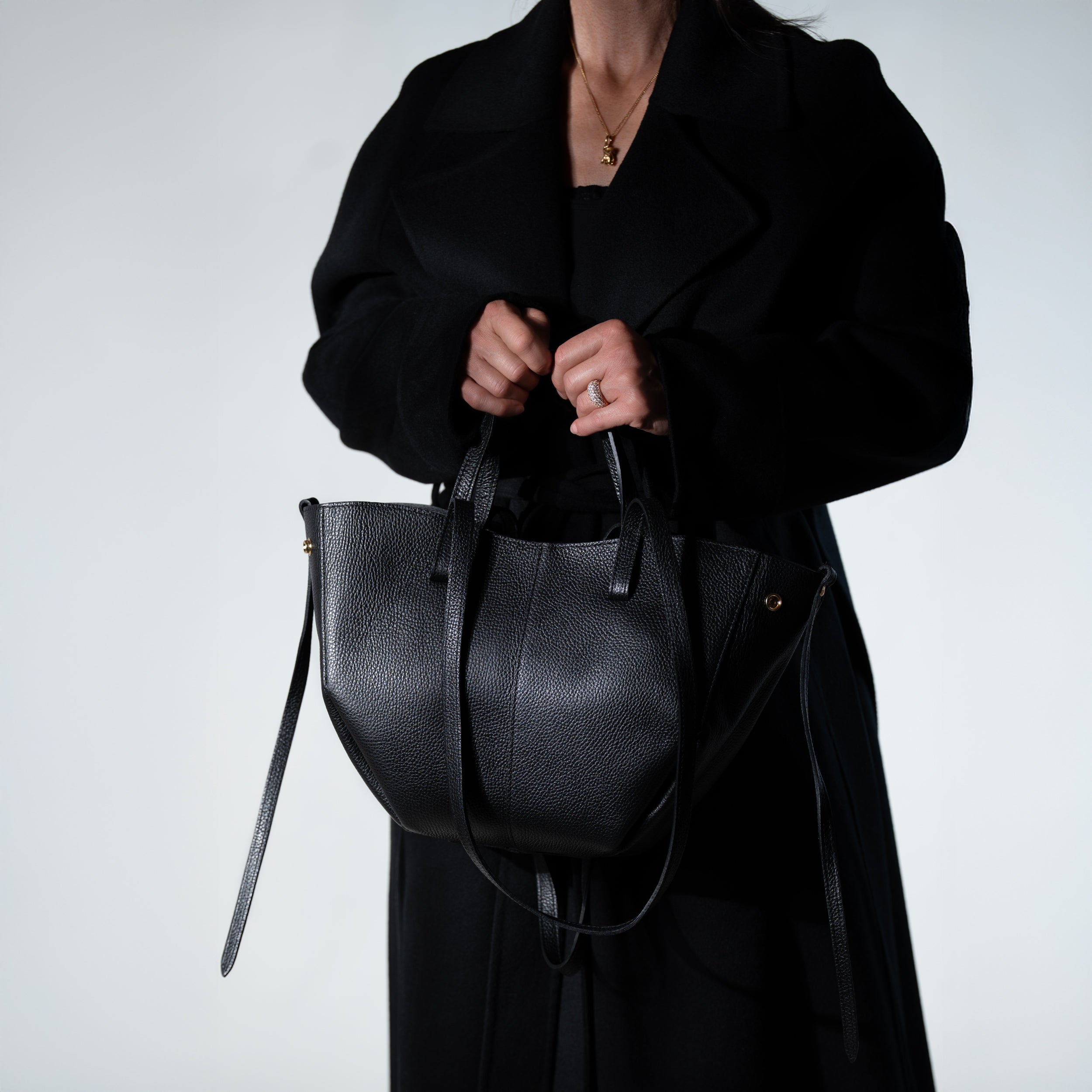 grand sac cabas pour femme forme trapèze en cuir lisse noir porté main avec manteau noir