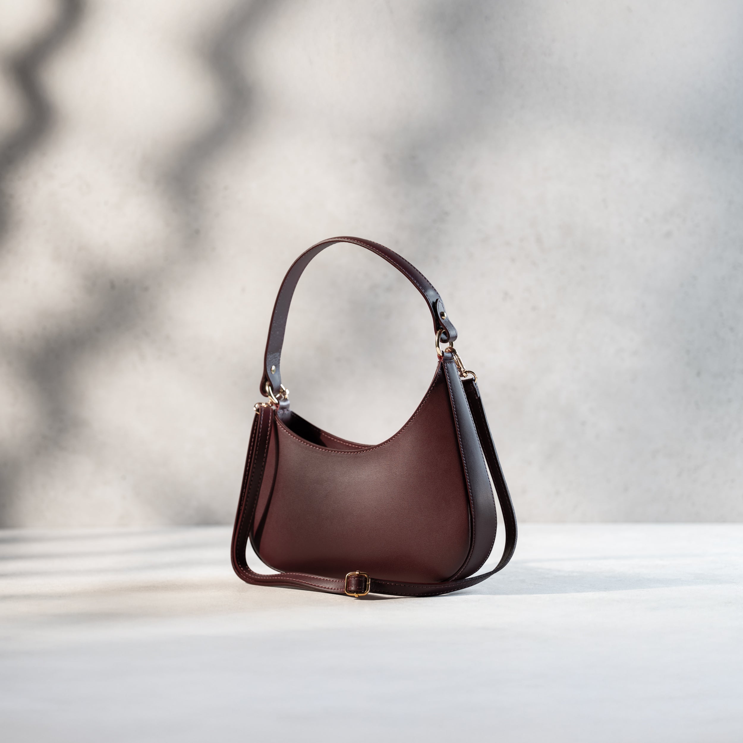 sac à main forme hobo demi lune asymétrique pour femme en cuir lisse bordeaux avec bandoulière de côté