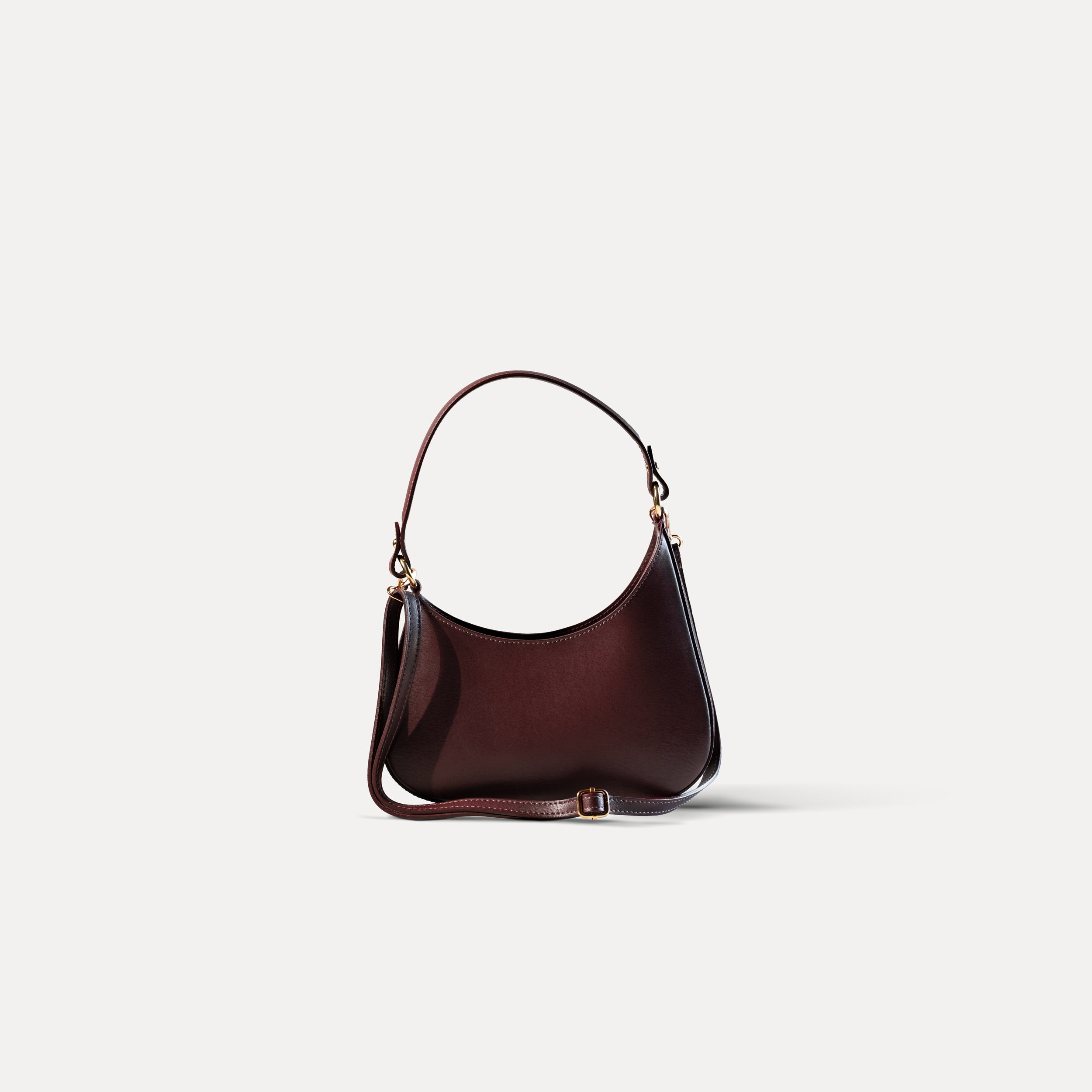 sac à main forme hobo demi lune asymétrique pour femme en cuir lisse bordeaux avec bandoulière sur fond blanc