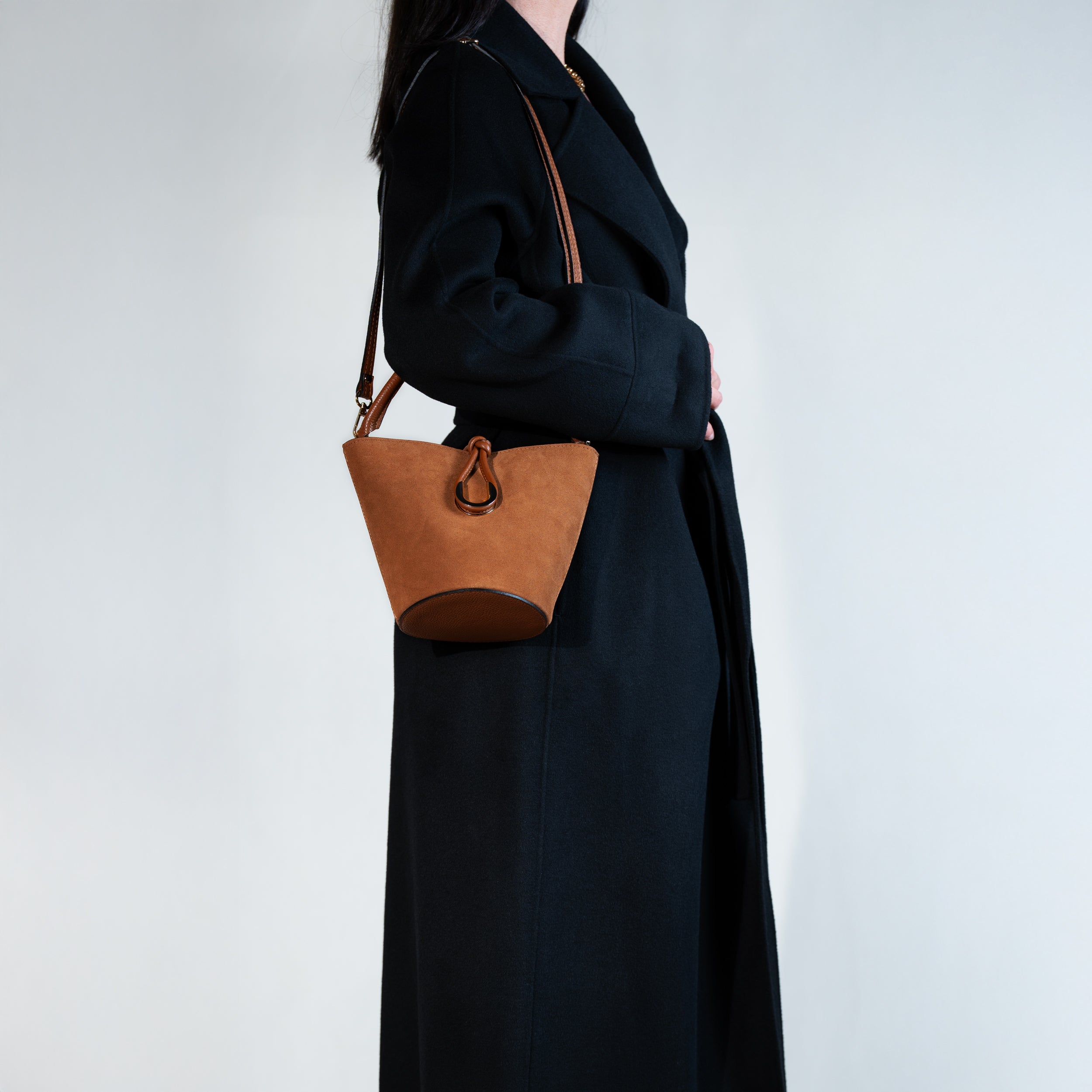 sac à main femme en cuir suédé ou daim camel en forme seau porté en bandoulière avec un fermoir doré original sur un manteau noir