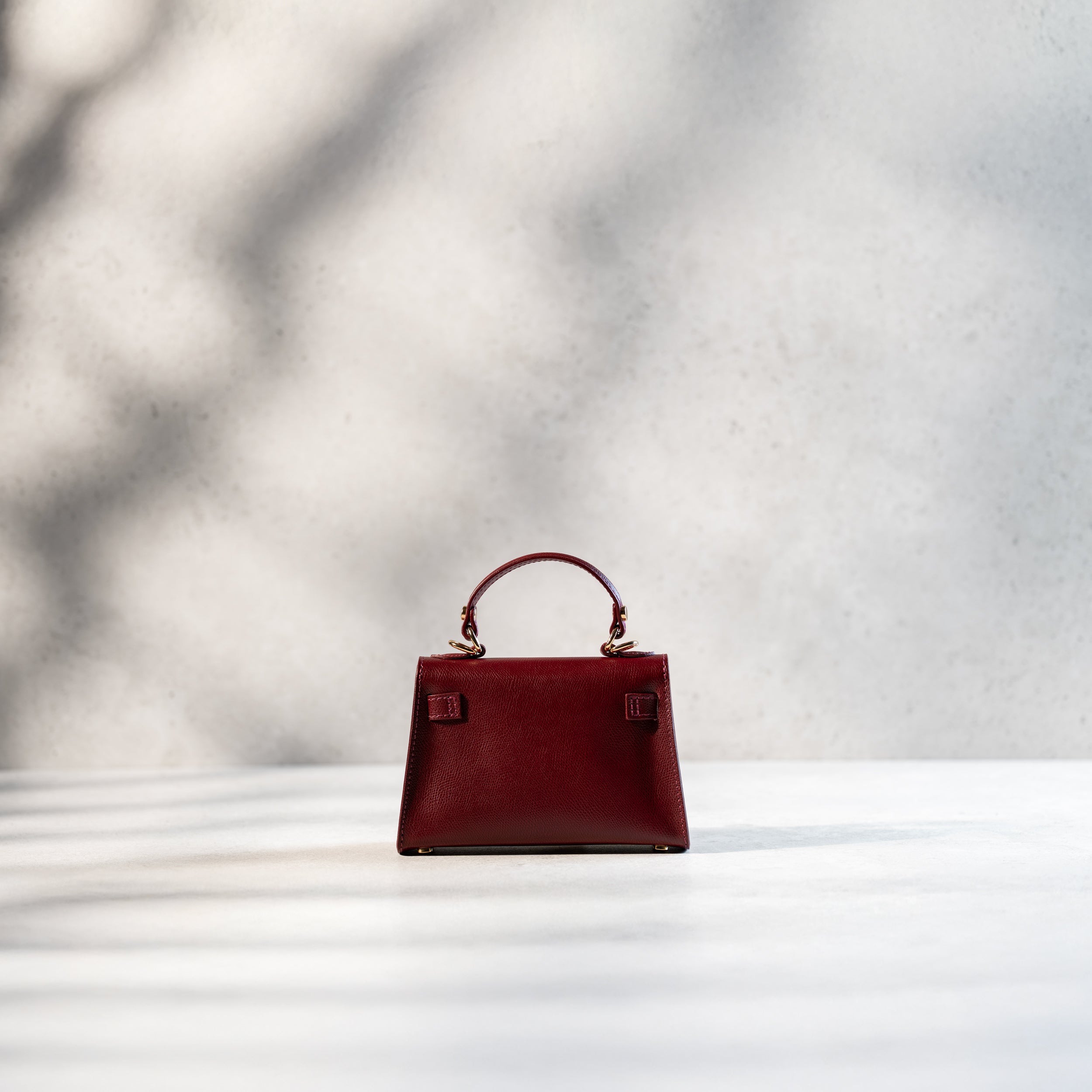 arrière d'un sac à main femme en cuir saffiano bordeaux top handle avec une bijouterie doré et des clous de fond de sac 
