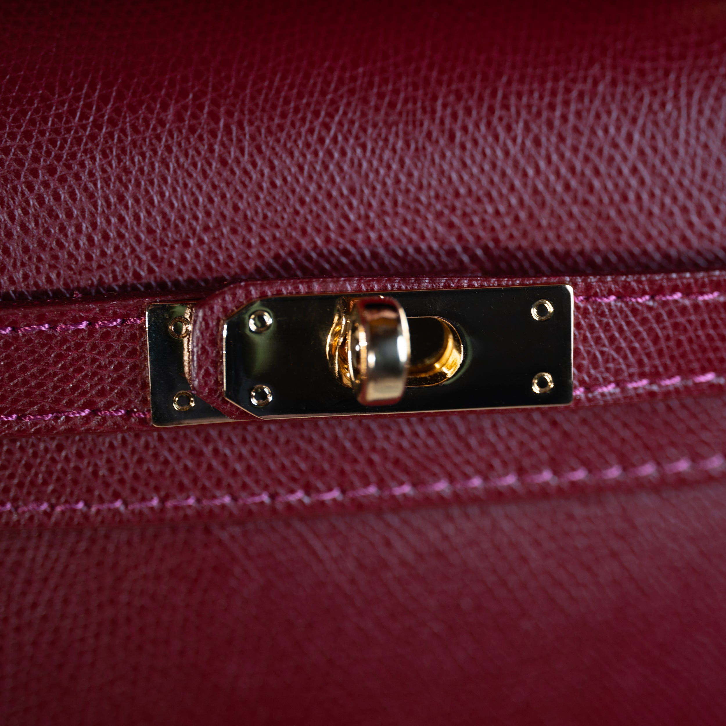 zoom sur le cuir saffiano d'un sac à main top handle avec focus sur son fermoir tourniquet doré et son cuir de qualité bordeaux 