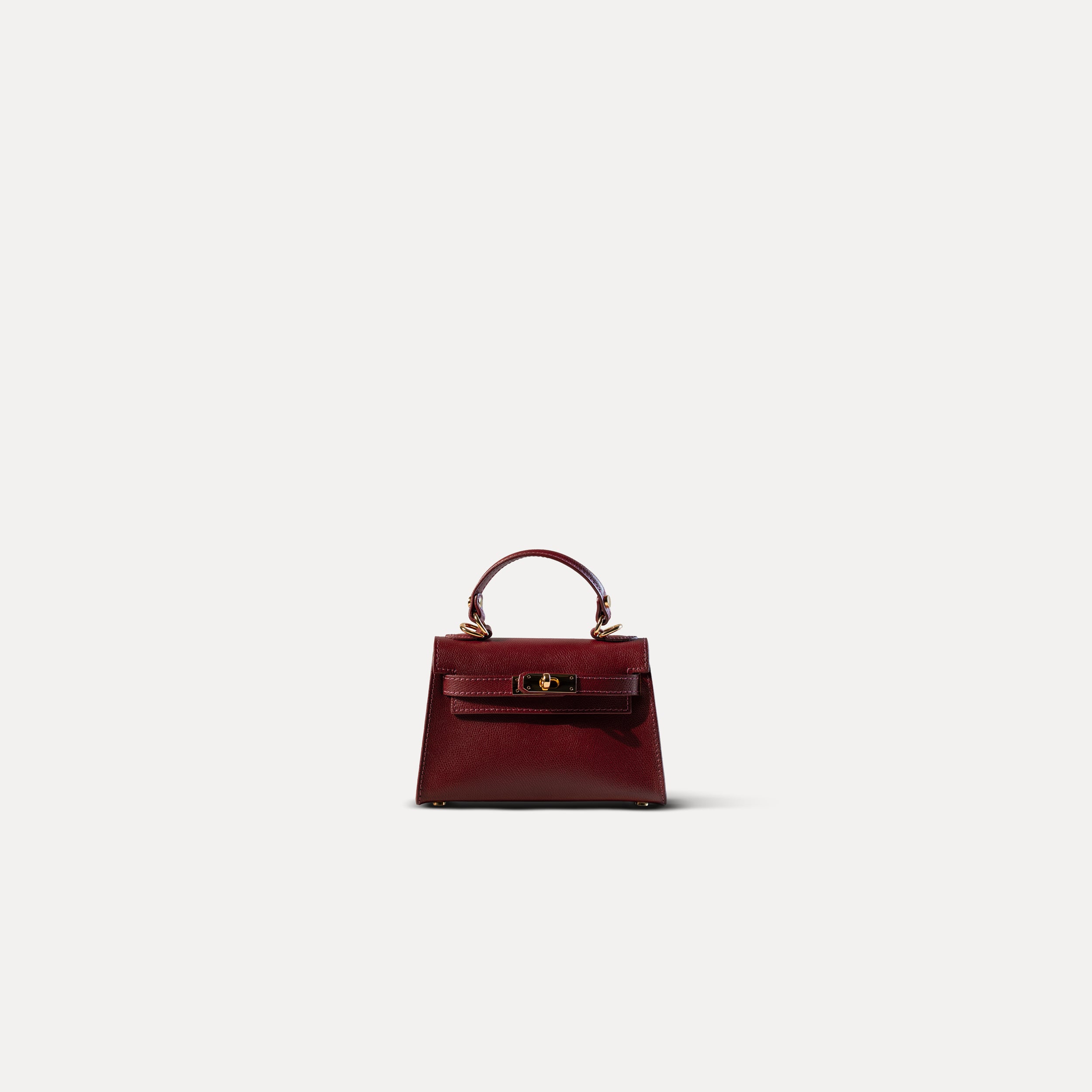 sac à main femme en cuir saffiano bordeaux top handle avec une un fermoir tourniquet, une bijouterie doré et des clous de fond de sac sur un fond blanc